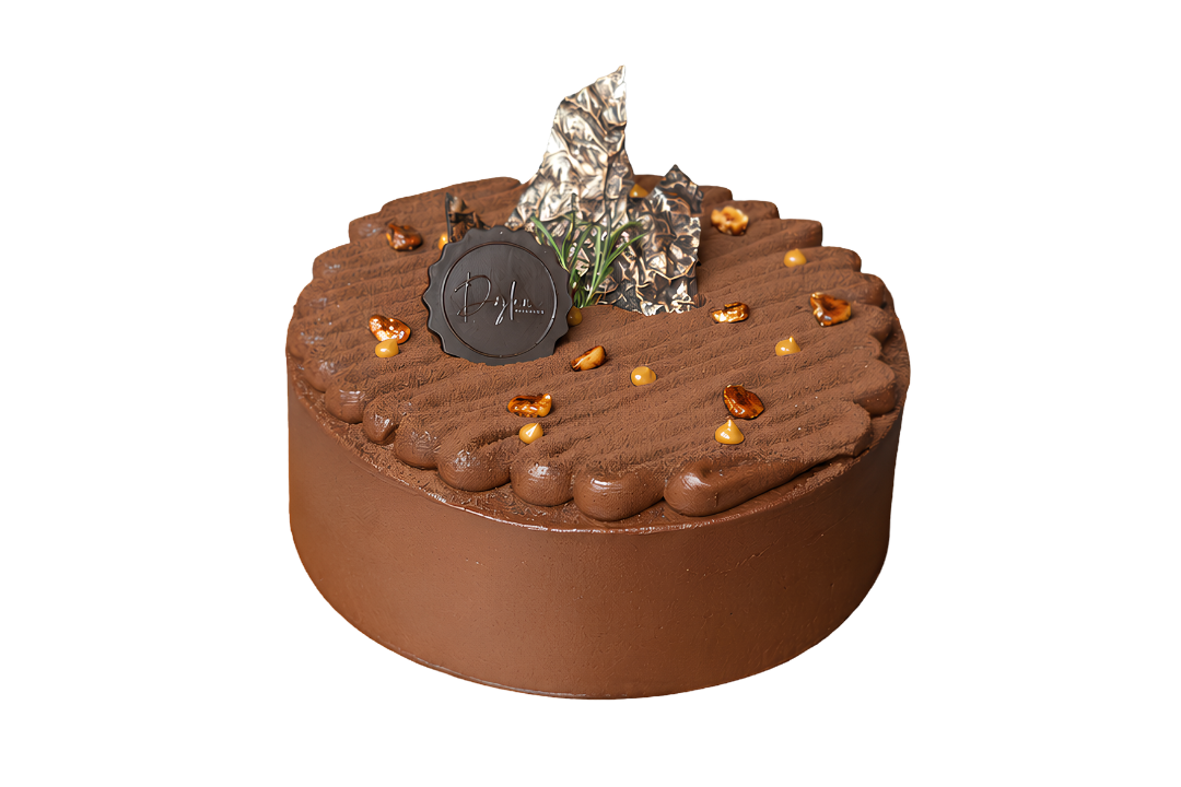 A round chocolate cake with a smooth milk-chocolate finish, piped decorative borders, scattered amber-colored jewel-like decorations, and a dark chocolate medallion on top, isolated on a white background.