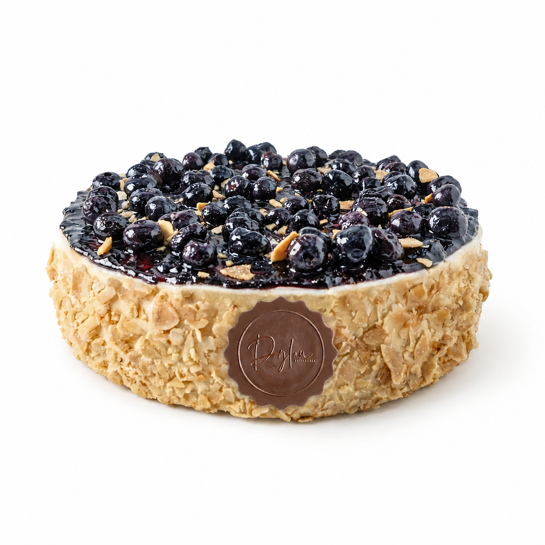 A round blueberry cheesecake with a crumbly oatmeal-like crust, topped with fresh blueberries and chopped nuts, featuring a chocolate plaque with the brand name &
